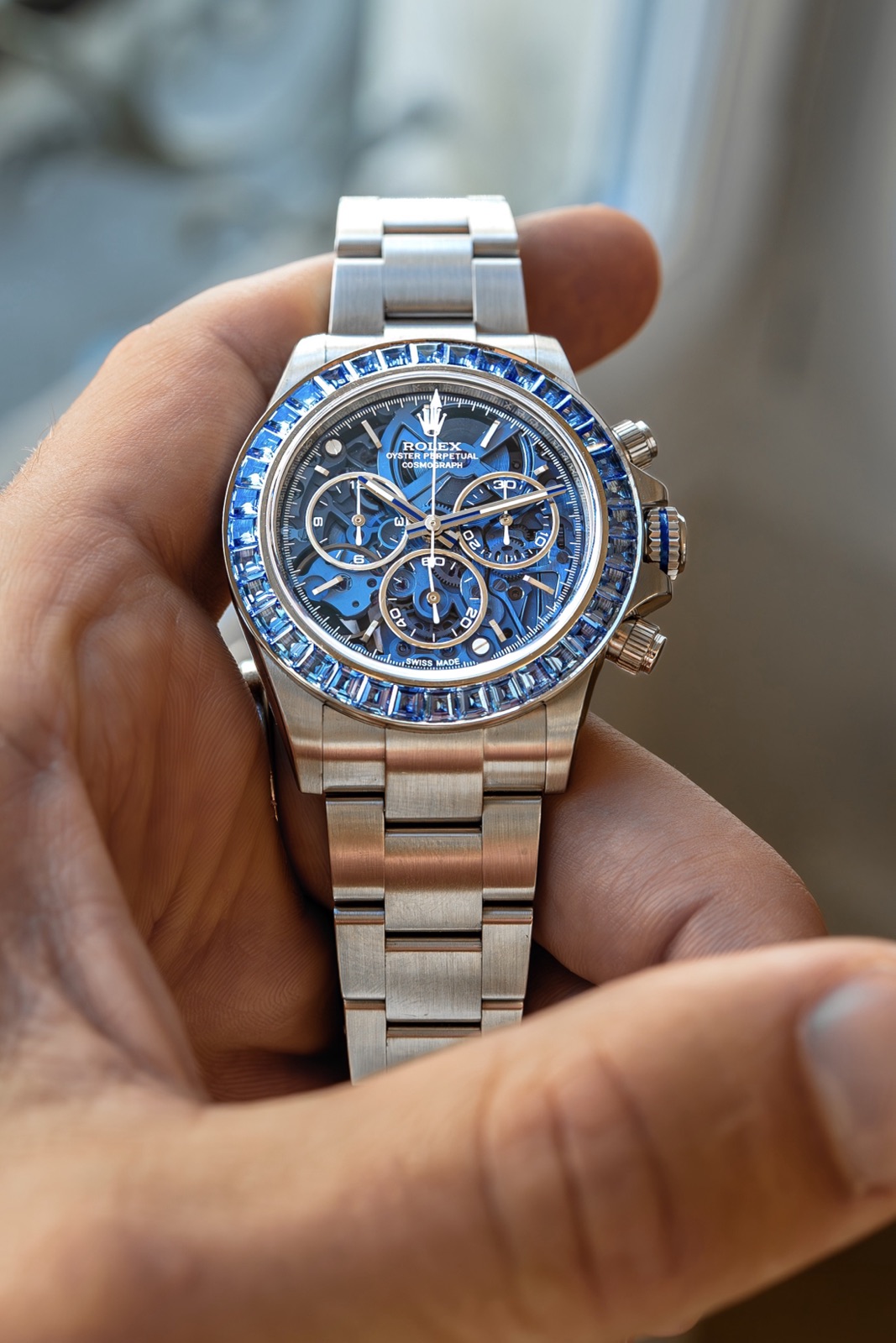 A skeletonised Rolex Daytona with a translucent blue sapphire dial and a blue-sapphire-set bezel, held in a hand