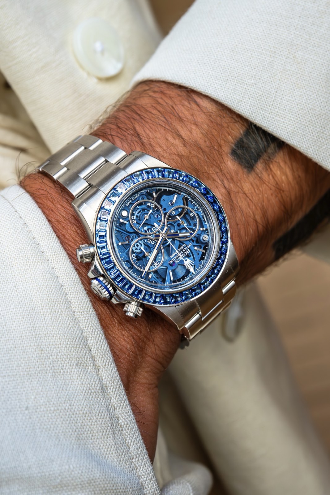 The Arolla Daytona under a pale jacket cuff on a steel bracelet, with a blue band around its steel crown