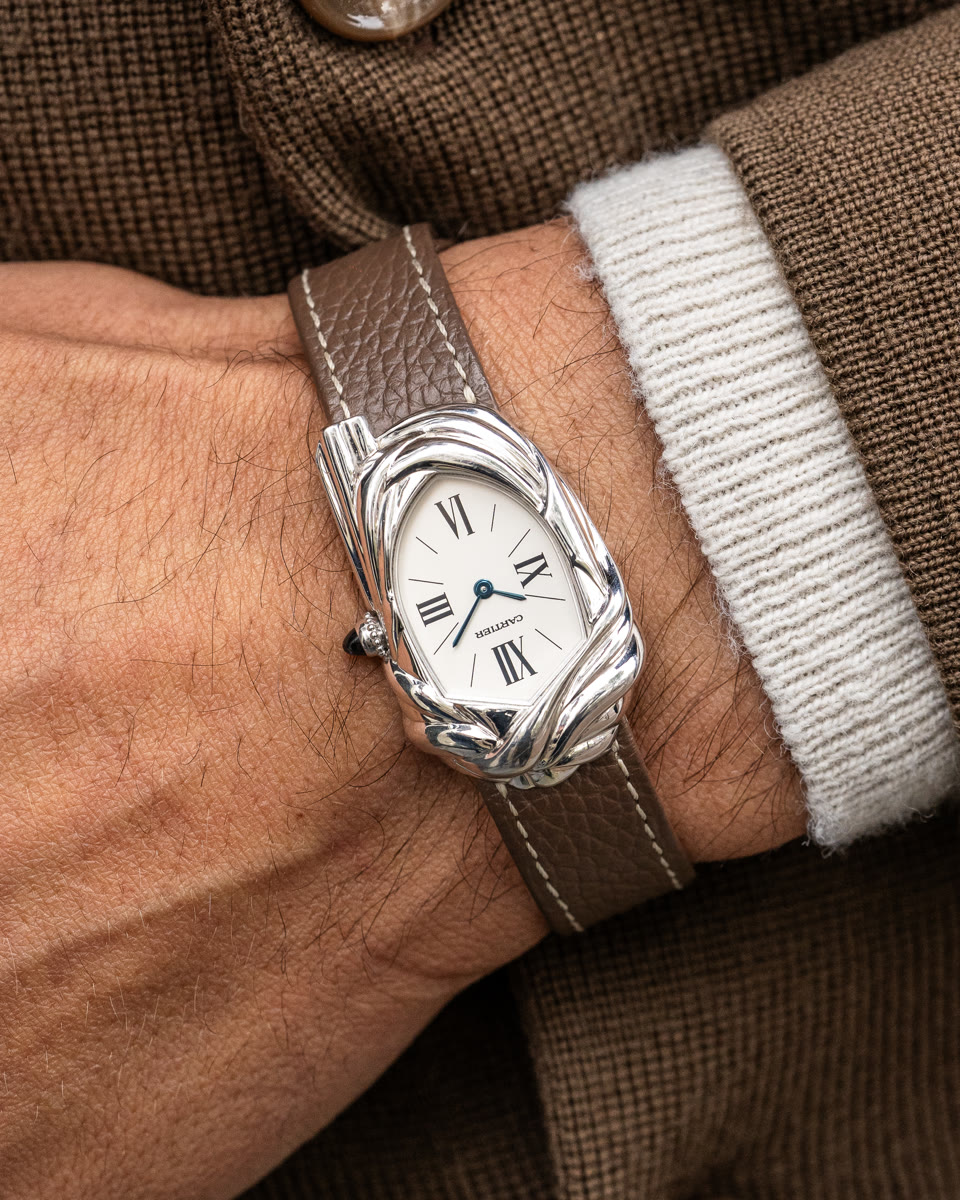The white-gold Cartier Cheich on a wrist beside a ribbed cuff, its woven case around a small white dial