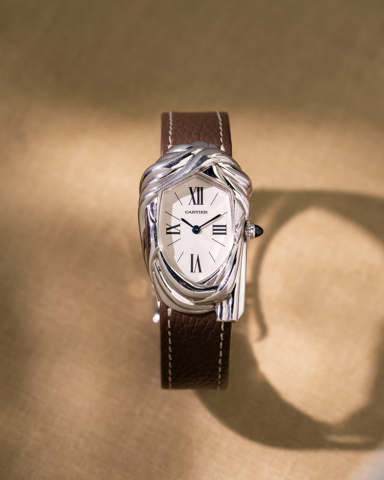 The whole white-gold Cheich on linen, its brown strap curving away from the case