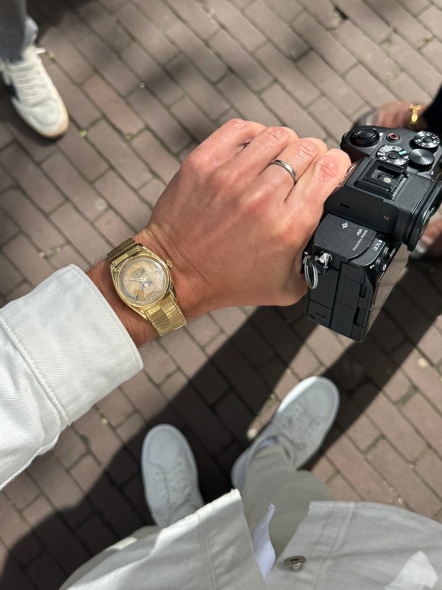 Jimmy Heneidy holding a Sony camera, with a gold watch visible on his wrist, on an Amsterdam street
