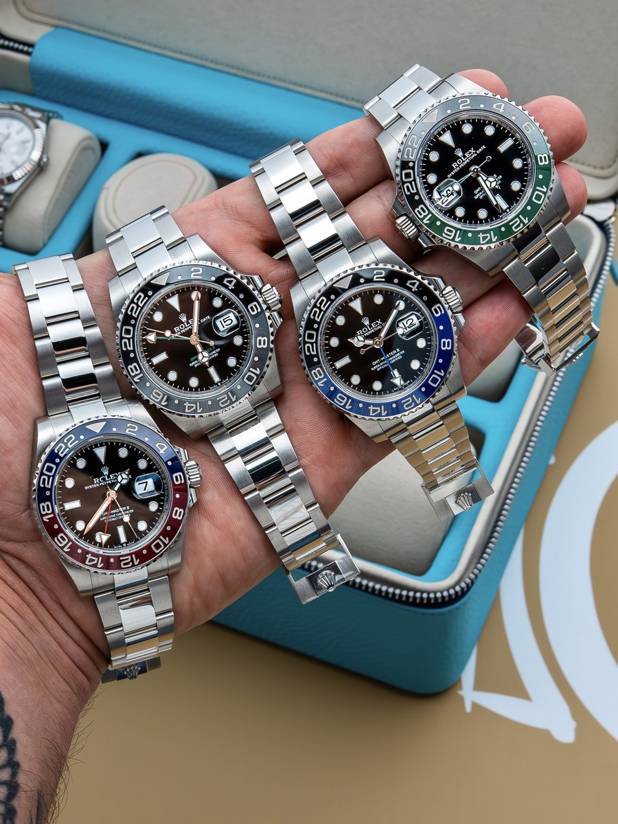 Four Rolex GMT-Master II watches arranged across a hand above an open blue watch case