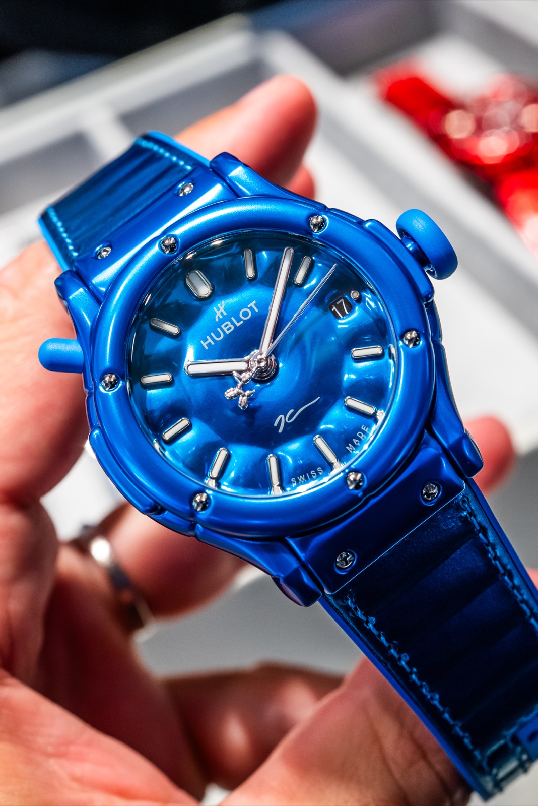 Blue Hublot watch held close to the camera, with straight baton markers and a signature visible on the dial