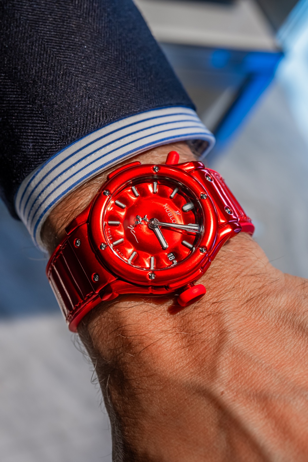 Red Hublot watch on a wrist, seen at an angle beneath a striped shirt cuff