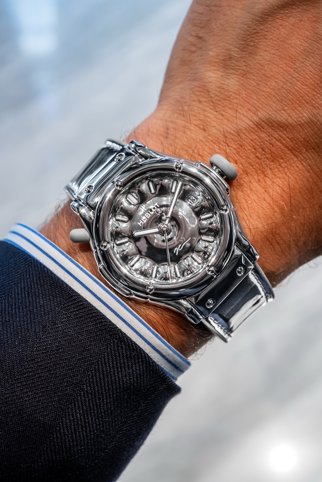Reflective silver Hublot watch photographed on a wrist, with pale rounded controls and a mirror-bright strap