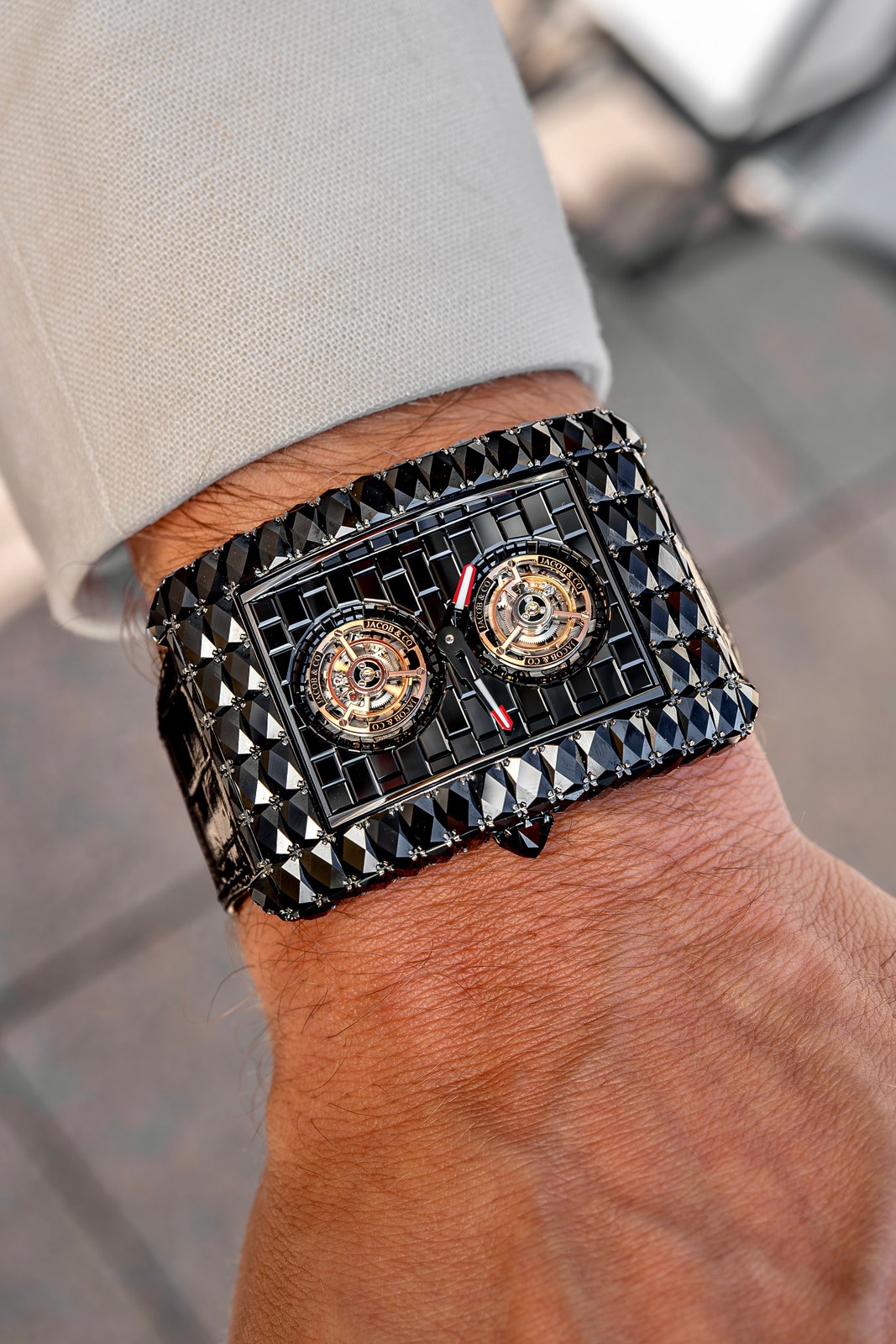 The black-treated-diamond Angel-Cut on a wrist under a cream jacket, the whole watch dark, the tourbillon cages and red-tipped hands visible