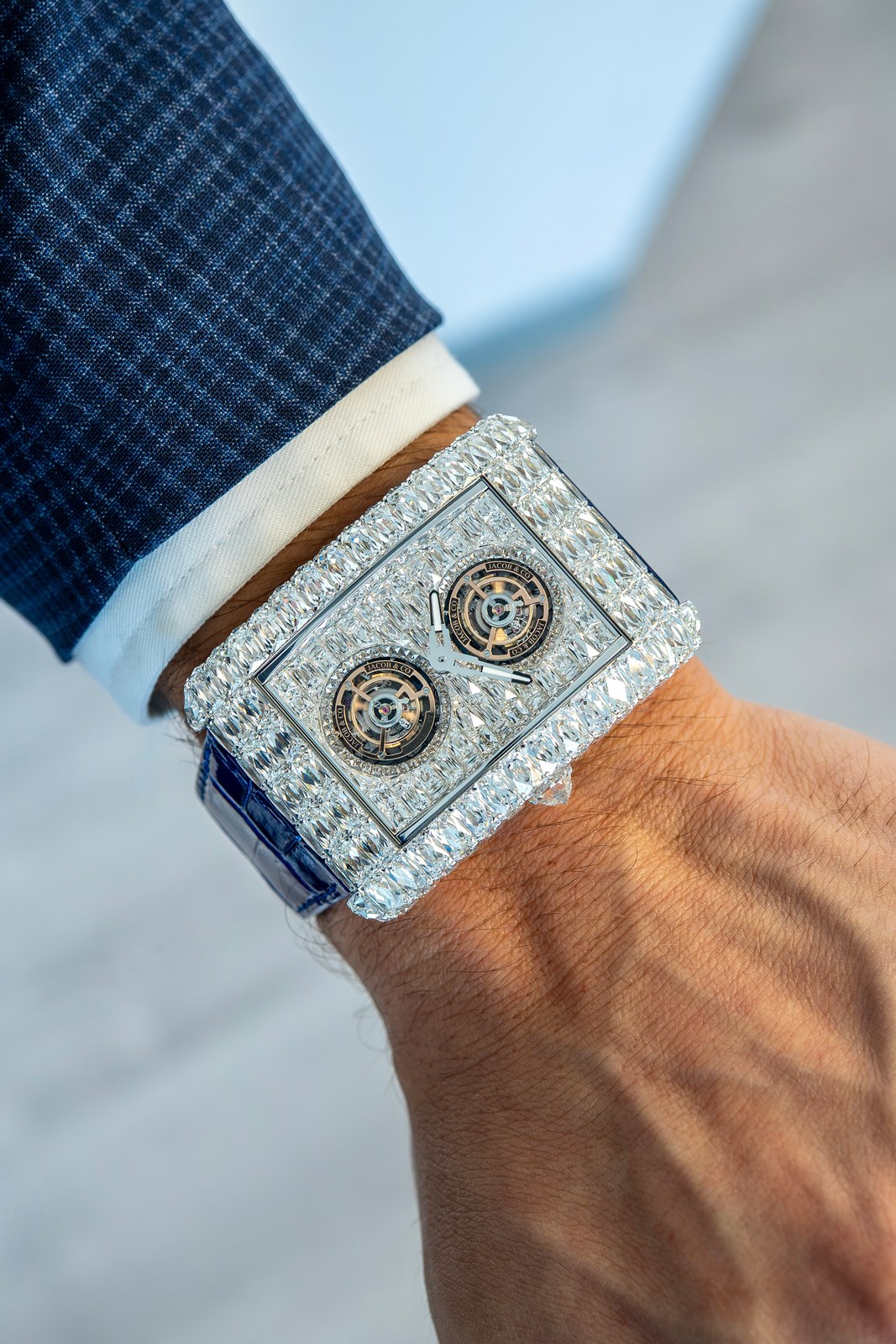 The white-diamond Angel-Cut beside a blue checked jacket cuff, with its set case flank and two tourbillon openings visible