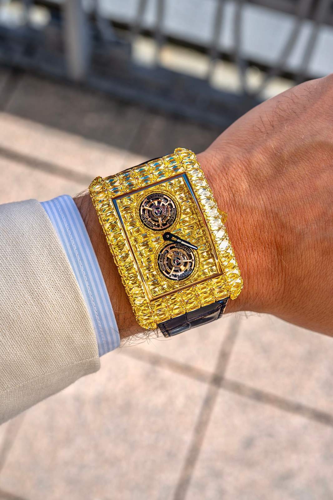 The yellow-diamond Angel-Cut on a wrist beside a beige jacket cuff and a striped shirt, the rectangular case and dial set with yellow stones around two tourbillons
