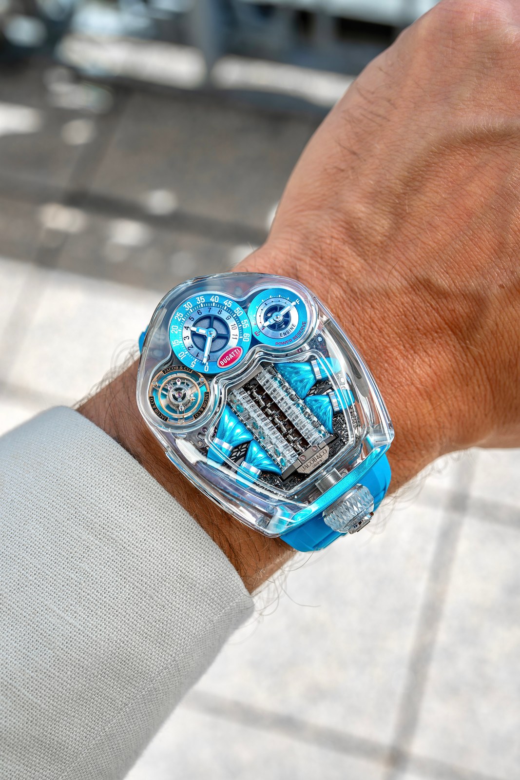 The Bugatti Tourbillon Sapphire Crystal in clear and blue on a wrist: transparent case, the sapphire engine block with blue manifolds either side, two blue-rimmed counters, blue rubber strap