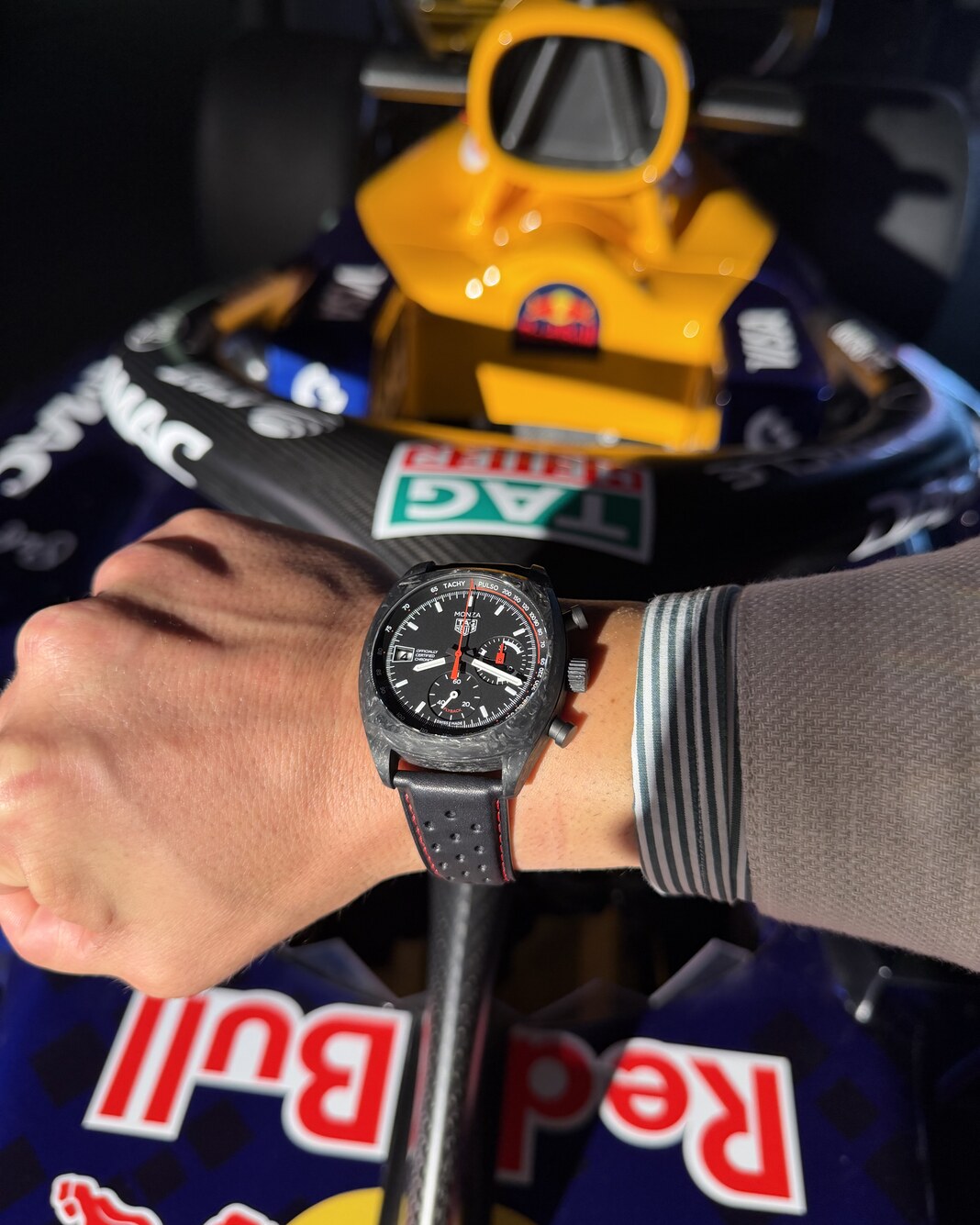 A TAG Heuer Monza with a dark, mottled case worn in front of an Oracle Red Bull Racing car carrying a TAG Heuer logo