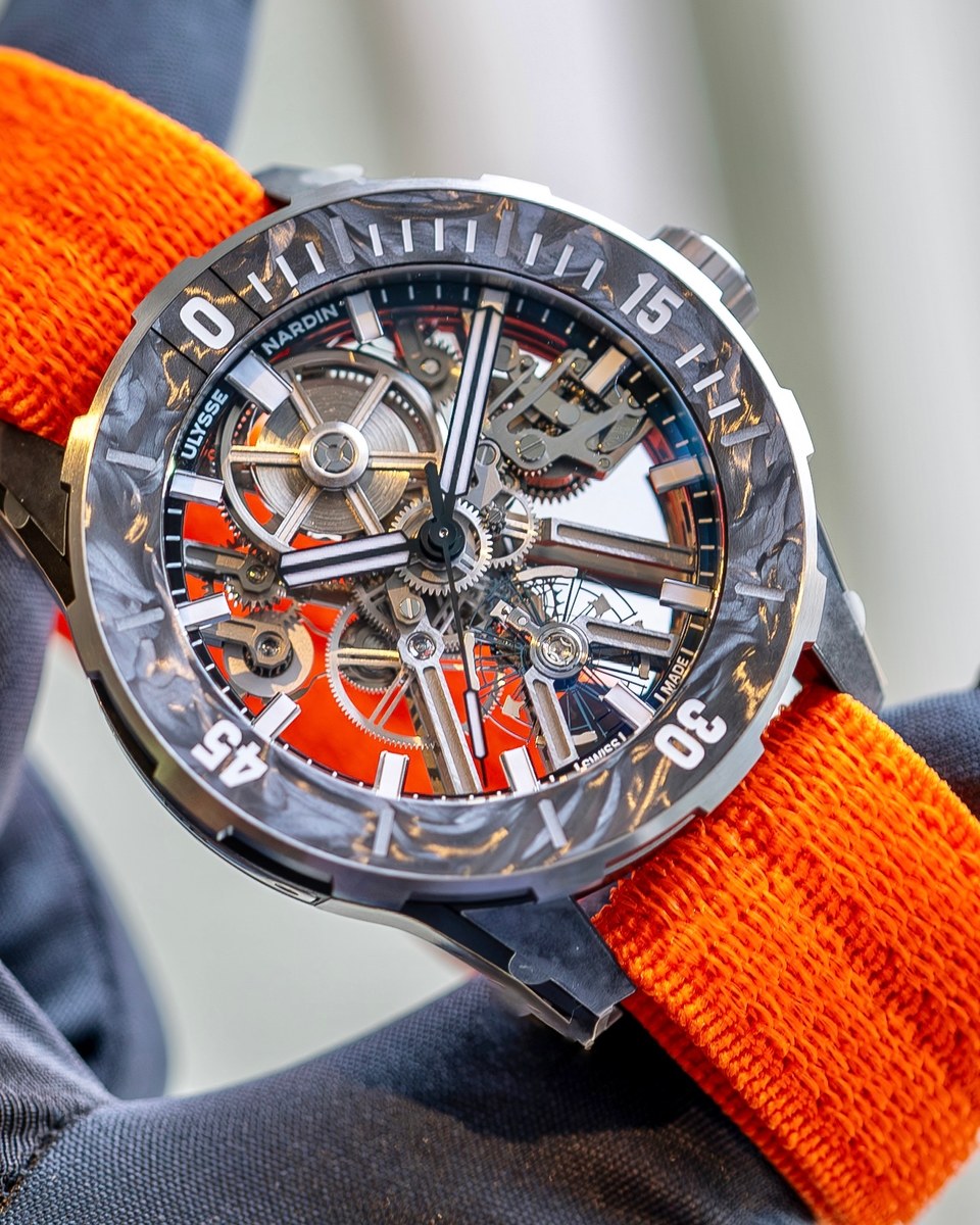 Ulysse Nardin Diver [AIR] held up close: carbon bezel, skeletonised movement over an orange base plate, orange fabric strap