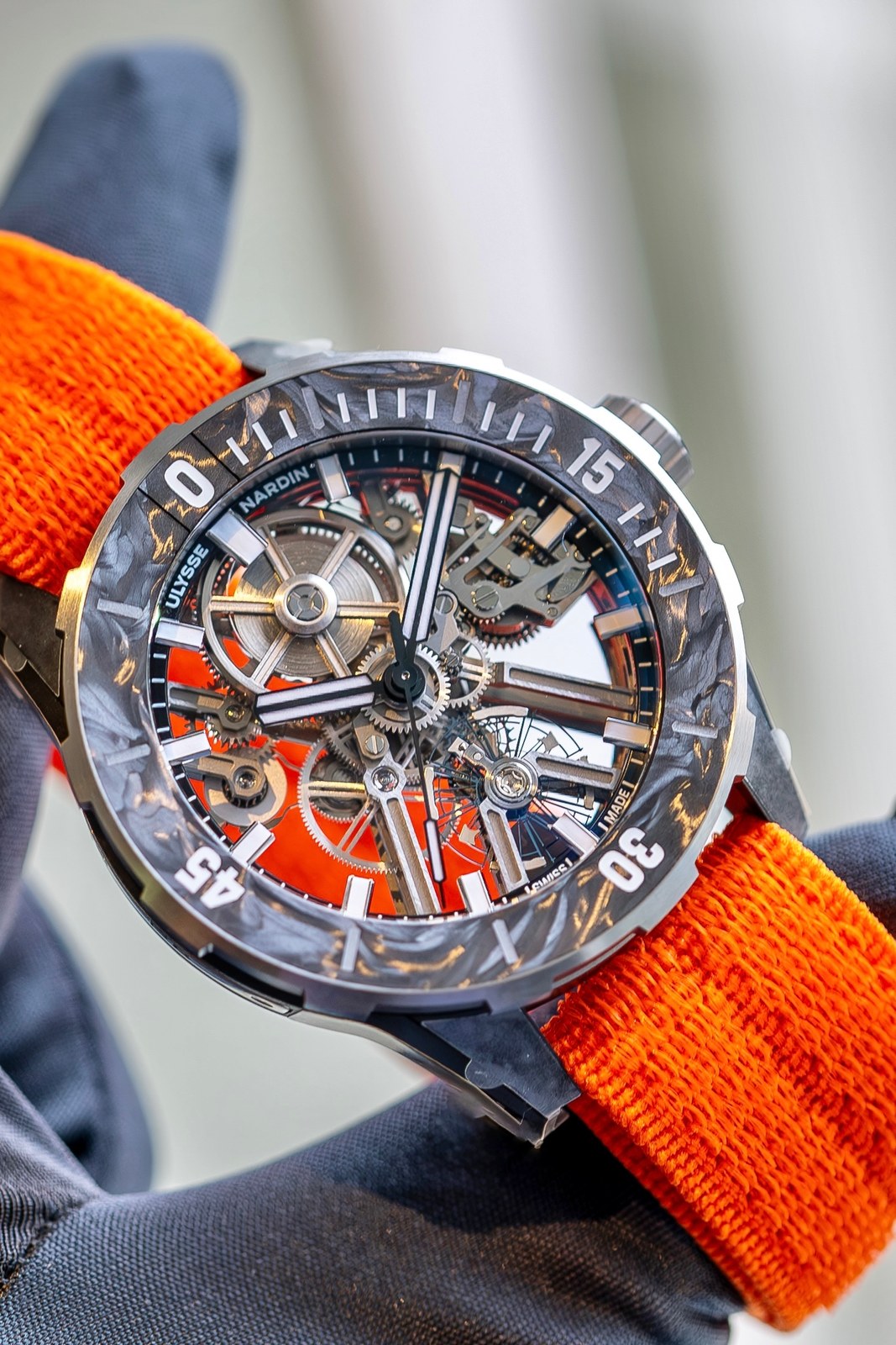The Diver [AIR] held in a dark-gloved hand, the mottled CarbonFoil bezel and the orange strap close up