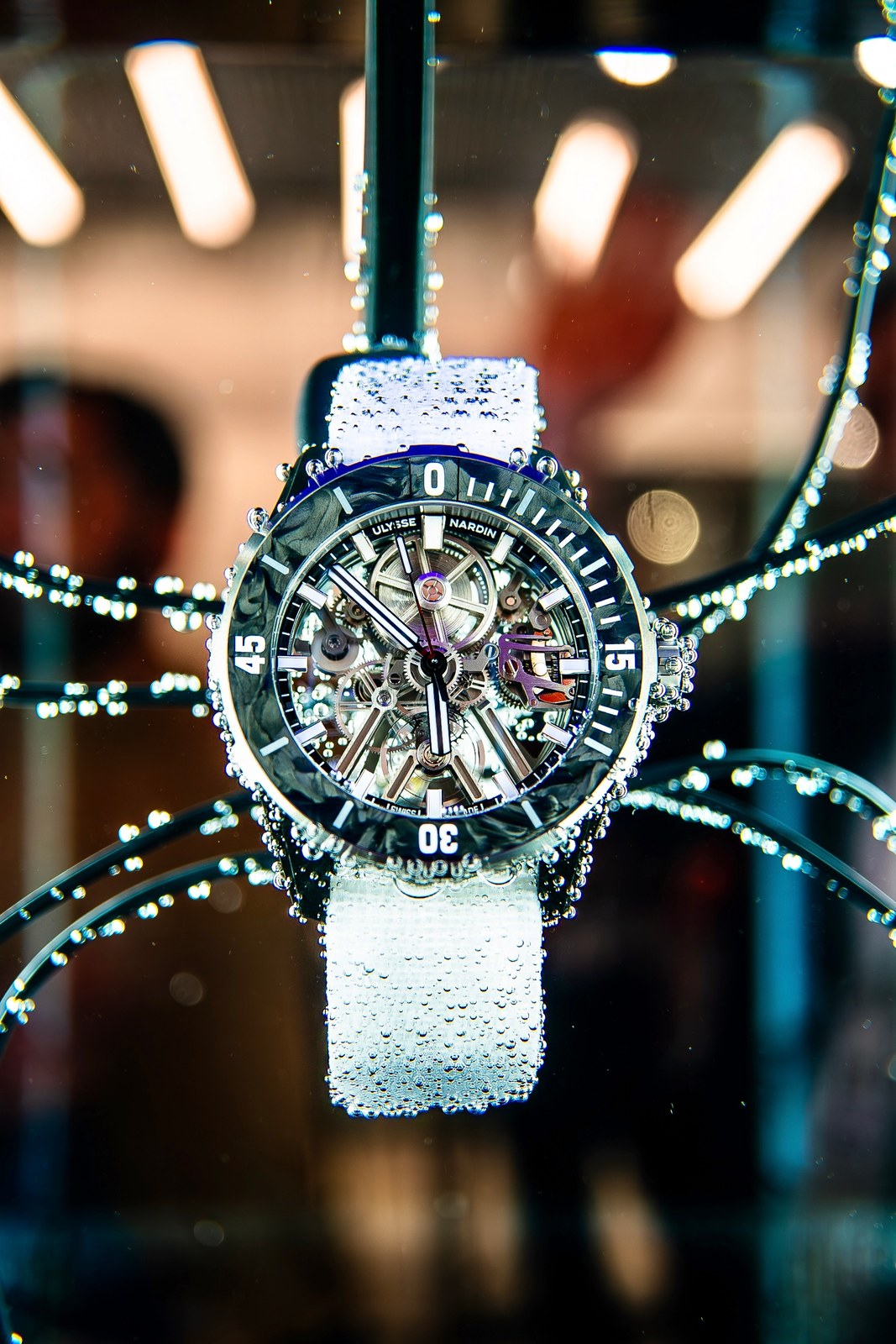 The Diver [AIR] on its white strap suspended inside a dark display case, droplets on the strap and case