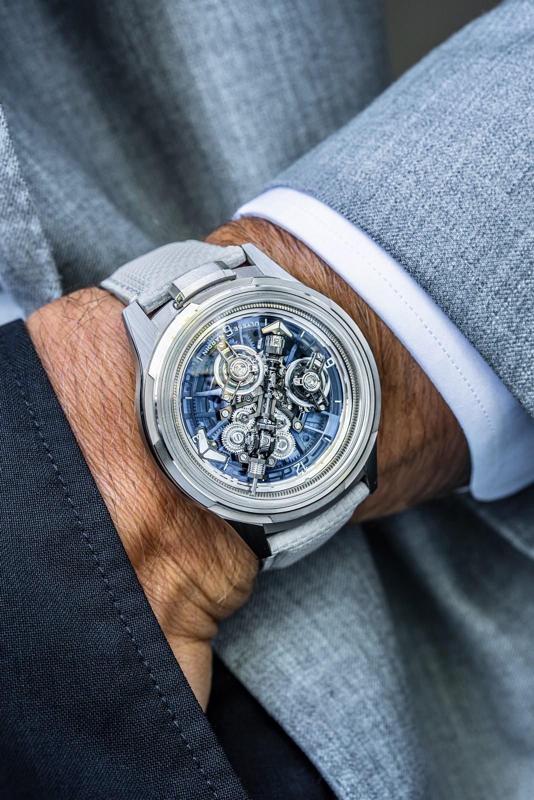 Ulysse Nardin Super Freak on a wrist beneath a grey jacket sleeve and white cuff, with the blue open display and twin tourbillons visible