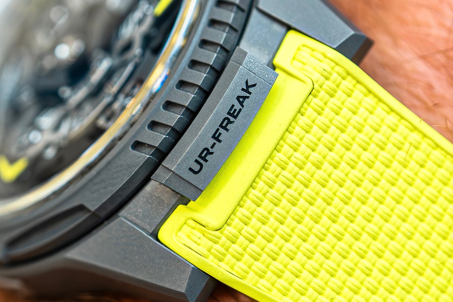 Close view of the UR-FREAK's case edge: the fluted titanium bezel, the locking tab marked UR-FREAK and the yellow textured strap